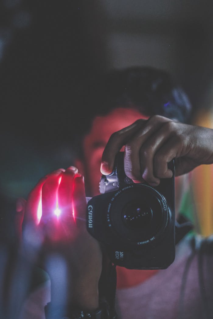 services-02 Close-up of a photographer holding a DSLR, captured in dim light.