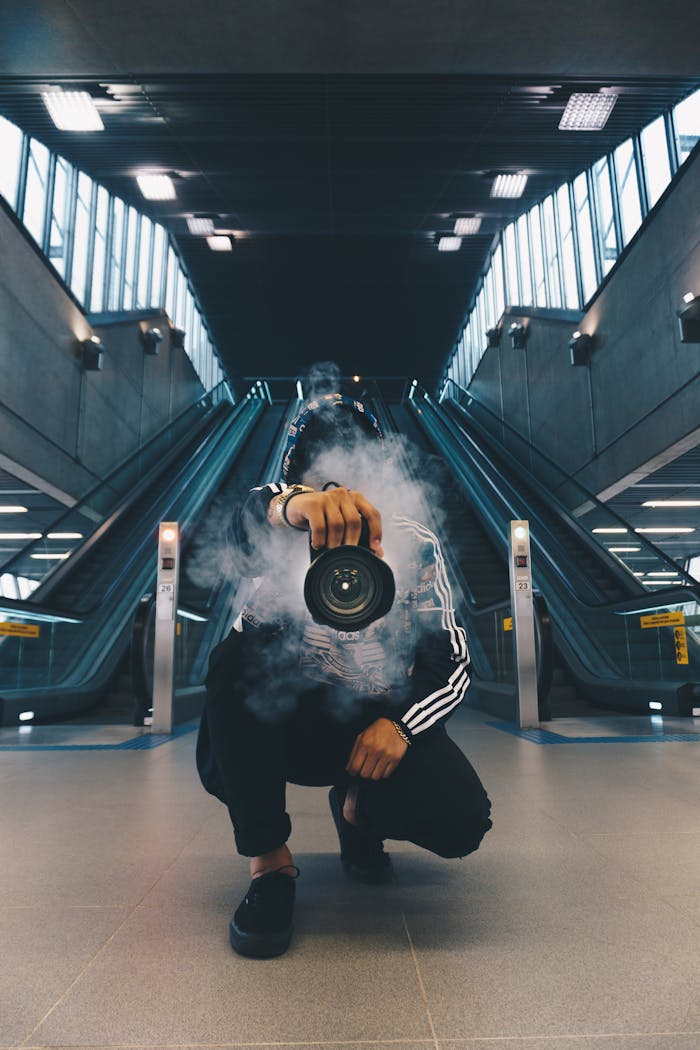 gallery-01 Person holding a camera in a smoke-filled urban setting with escalators.