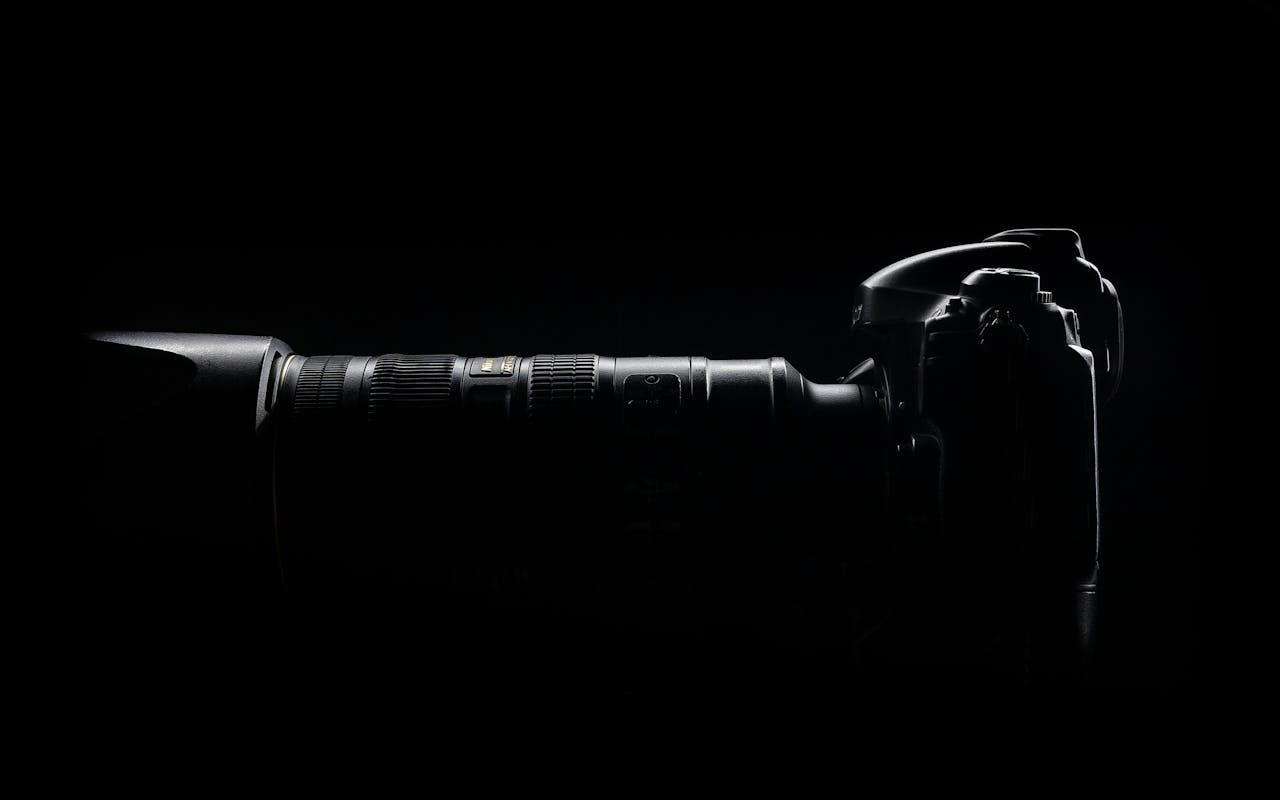 services-01 Artistic side profile of a DSLR camera with lens in dark setting.